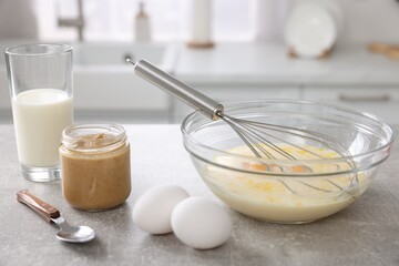 Wall Mural - Whisk, bowl, beaten eggs and other ingredients on grey table indoors