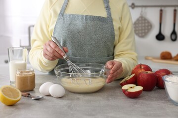 Wall Mural - Woman whisking eggs in bowl at grey table indoors, closeup