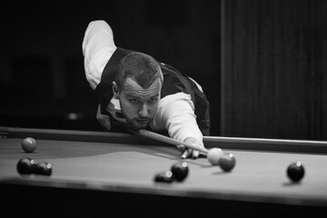 Focused young man leaning on billiards table, aiming cue on balls, playing snooker game. Online course banner for mastering billiards skills. Concept of billiards sport, gambling, hobby, leisure, game