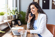 © Dragana Gordic - Smiling pretty skilled young woman with wireless earbuds sitting at table in office and working with modern computer. Happy businesswoman taking a video call in a co-working space