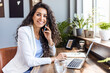 © Dragana Gordic - Focused young businesswoman using a laptop and wireless earphones while working alone. Young female entrepreneur working remotely in a modern co-working office.