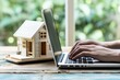 individual using a laptop with a tiny house model beside it