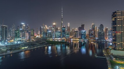 Wall Mural - Aerial panoramic view to Dubai Business Bay and Downtown with the various skyscrapers and towers along waterfront on canal day to night transition timelapse. Construction site with cranes after sunset