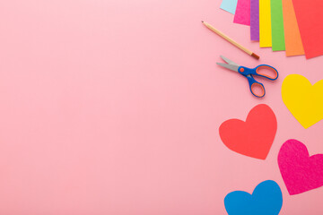 Wall Mural - Heart shapes, scissors, pencil and colorful application paper on light pink table background. Pastel color. Closeup. Making decoration elements. Empty place for text. Top down view.
