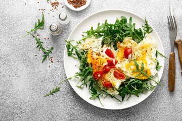 Wall Mural - Fried eggs, omelette with onions, tomatoes and fresh arugula salad, top view