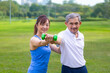 Senior asian man is using dumbbell for weight training strength while his daughter is supporting in the public park for elder longevity exercise and outdoor workout usage