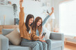 © oatawa - Exciting young asian women LGBT happy couple sitting on sofa using mobile phone in living room at home, Friendship concept