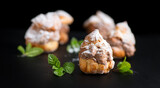 Fototapeta  - Profiteroles or cream puff with filling,  powdered sugar topping, on black background. Fresh homemade Cream Puffs, cake, tasty French choux puff, ecler, dessert closeup. Pastries