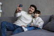 © F8  \ Suport Ukraine - Happy father and little son taking selfie by smartphone sitting on sofa at home