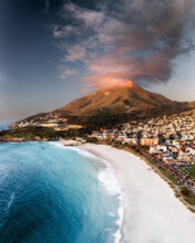 Aerial View Of A Mountain With A Dramatic Cloud Formation Above It And A White Sandy Beach With Blue Water In The Foreground, Cape Town, Western Cape, South Africa.