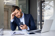 © Tetiana - Shocked young man businessman, lawyer, banker sitting in office at desk, holding hand to head and looking frustrated at phone screen
