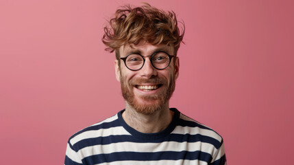 Canvas Print - A young man in glasses with a joyful expression and a casual striped shirt stands against a vibrant pink background.