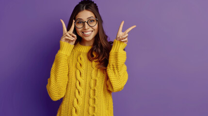 Poster - A cheerful young woman in a bright yellow sweater and stylish glasses makes a peace sign with her hand, smiling brightly against a purple background.