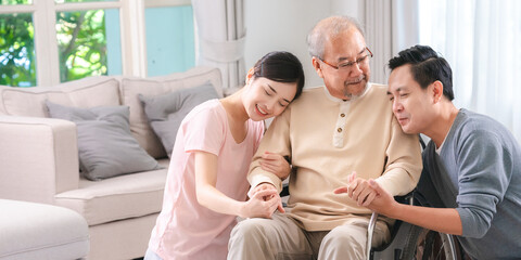 Happy elder Asian man using wheelchair while exercise indoor house with his son taking care of him at the retirement age with copy space