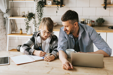 Wall Mural - family dad young man with phone and son teenage cute boy with tablet and headphones doing homework sit at table in cosy apartment, quality time with your family, gadget addicted, education