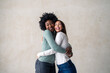 © Dorde - Two best friends smiling while embracing each other in a studio. Happy young women enjoying themselves while standing against a background in a studio.