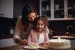 Mother and her daughter are happy while looking at the just baked cake.