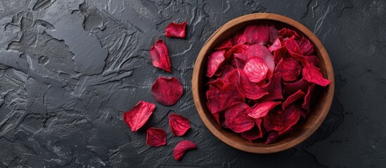 A wooden bowl filled with vibrant red petals sits atop a black table. The petals contrast beautifully against the dark surface, creating a striking visual display.