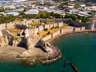 Wall Mural - Aerial view of medieval fortified Mamure Castle on shore of Mediterranean Sea against backdrop of agricultural village of Bozdogan with many greenhouses on sunny spring day, Turkey