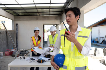 Wall Mural - Portrait of a male engineer at a construction site using a walkie-talkie. Standing in charge of planning a construction project in formal attire, wearing a hard hat, a successful civil engineer.