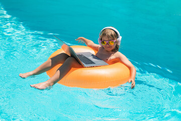 Wall Mural - Kid remote working on laptop in pool. Little business man working online on laptop in summer swimming pool water.