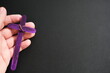 Human hand holding a purple wooden cross in black background. Nurture, care and love christian faith concept.