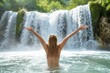 A joyful Woman with her hands up stands under the waterfall and enjoys the water of the waterfall on a sunny, hot day. The atmosphere of pleasure, freedom, happiness. 