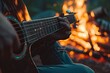 A close-up of a person's hands strumming a guitar by a campfire illustrating the informal and intimate moments of musical expression. 