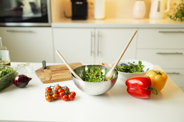 A bowl with a salad of fresh vegetables, tomatoes, arugula and spinach on the kitchen table. Healthy vegetarian salad on the white table in the kitchen