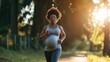 © mariiaplo - A pregnant African American woman enjoys jogging in a sunlit park.