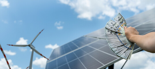 Poster - hand with dollar as saving against solar panels with wind turbines