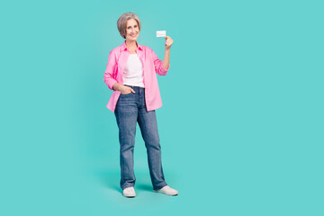 Wall Mural - Full length photo of cheerful woman wear pink shirt denim pants holding credit card hand in pocket isolated on teal color background