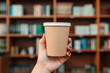 a woman holding a large recyclable kraft paper cup in a library