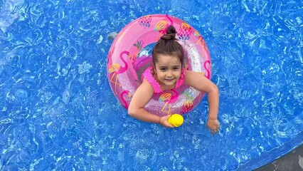 Wall Mural - Happy little girl relaxing in swimming pool, floating on pink inflatable ring. Traveling and vacation concept. Summer time. Top view