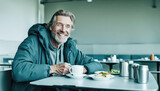 Fototapeta  - A homeless smiling middle-aged man sits at a table in a shelter and has lunch. Caring for homeless people