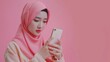 beautiful asian women in hijab holding and playing smartphone, sending short messages on the internet with someone, playing social media with feelings of pleasure.