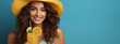 Radiant young woman with curly hair wearing a yellow hat enjoys a refreshing orange juice, exuding summer vibes and positivity