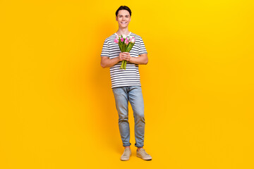 Sticker - Full length photo of good mood guy wear stylish t-shirt jeans pants holding tulips prepare for date isolated on yellow color background