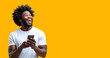 © Shyla Marsare - Hombre afro sorniente utilizando su smartphone. Hombre negro sobre fondo amarillo. Persona utilizando tecnología.