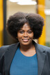 © JoseIMartin - A cheerful African American woman with a natural afro hairstyle wearing a smart blazer and blue sweater, indoors.