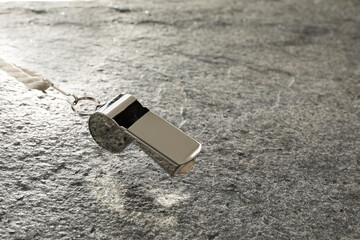 Wall Mural - Referee equipment. Metal whistle on grey textured background, closeup and space for text