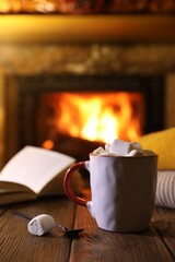 Sticker - Mug with hot cocoa, marshmallows and book on wooden table near fireplace