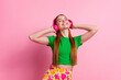 Photo of satisfied woman with ginger hair dressed green t-shirt touch headphones enjoy chill playlist isolated on pink color background