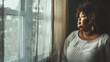 copy space, stockphoto, Plus size Black Woman standing in front of a window. Beautiful woman standing in front of a window in her home, watching outside. Big is beautiful. Body inclusive theme. Heavy 