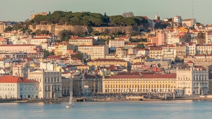 Wall Mural - The Commercial Square with crowd aerial timelapse, Castle Hill and Alfama district of Lisbon, Portugal viewed from Almada over Tagus river. Historic buildings with warm sunset light. Yachts floating