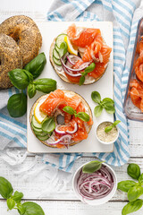 Poster - Salmon sandwiches with bagel, salted fish, fresh cucumber, onion and basil on white background, top view. Healthy breakfast with salmon toasts