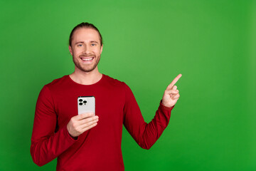 Wall Mural - Photo of intelligent man dressed red pullover hold smartphone indicating at proposition empty space isolated on green color background