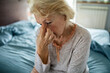 Distressed Senior Woman Sitting on Bed with Head in Hands