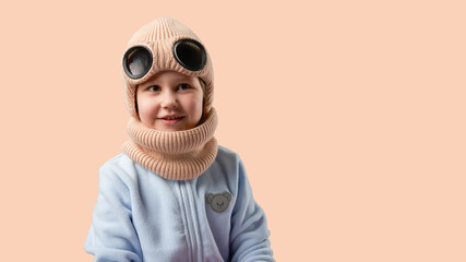 Wall Mural - Children's hats for cold weather. Happy smiling baby wearing warm hat with scarf on beige background. Copy space.           