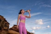 Woman Drinking Water From A Bottle Relaxing After Working-out, Mountain And Red Rocks Background